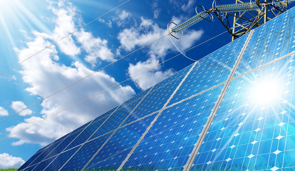 Solar panels under a bright sky connected to a power transmission tower